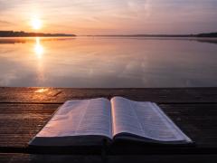 Bible on a table with a lake in the background at sunset