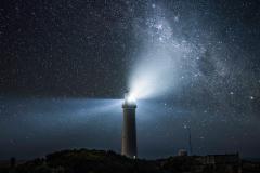 A lighthouse with a bright light against a starry sky